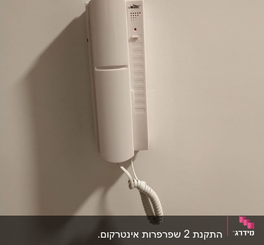אינטרקום לבן תלוי על קיר עם שפופרת